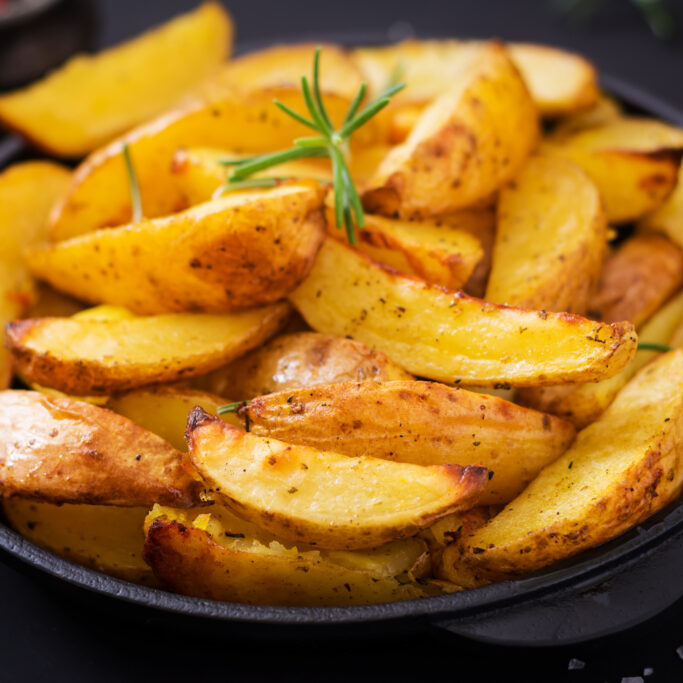 Ruddy Baked potato wedges with rosemary and garlic on a dark background.